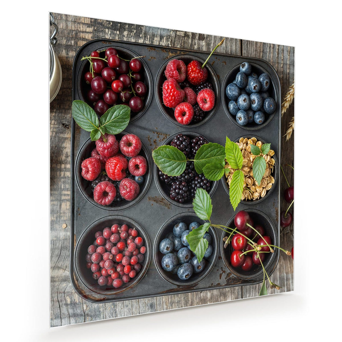 Muffinblech, dessen Mulden mit Kirschen, Himbeeren, Blaubeeren, Brombeeren, Johannisbeeren und Haferflocken gefüllt sind, auf Holz