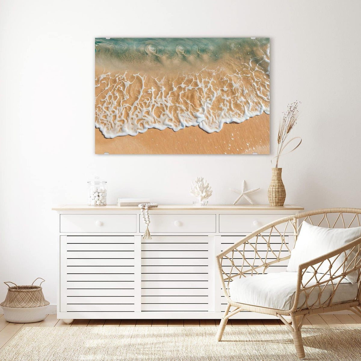 Wandbild aus Glas Meeresschaum auf Sand über einem weißen Sideboard neben einem Rattansessel