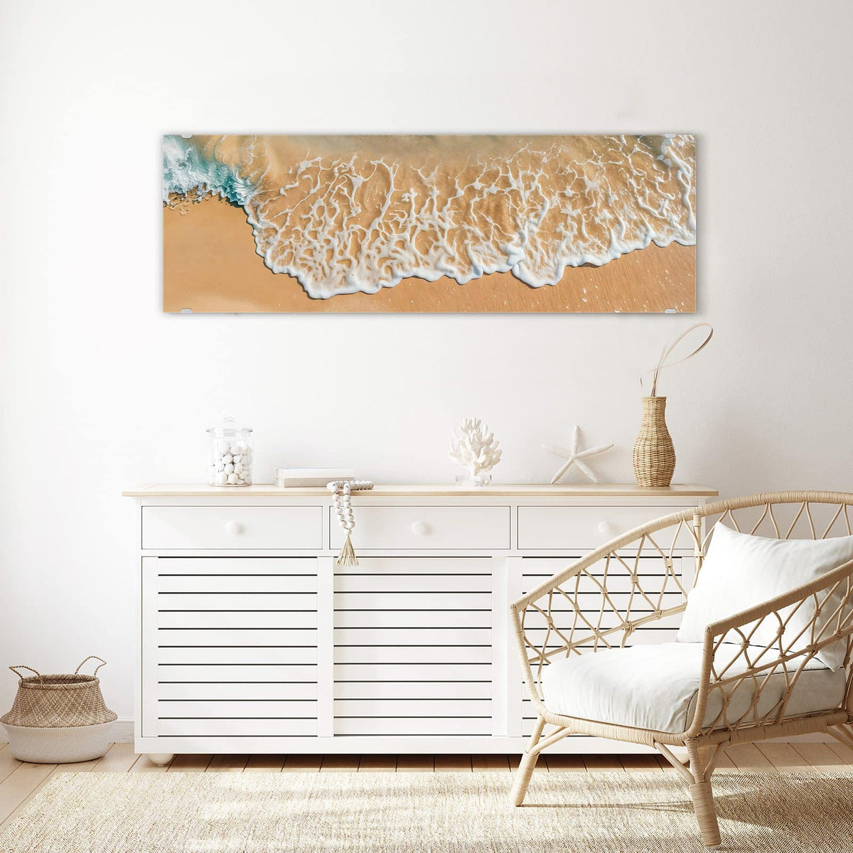 Wandbild aus Glas Meeresschaum auf Sand über einem weißen Sideboard neben einem Rattansessel