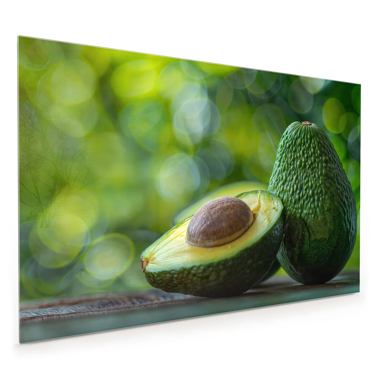 Küchenrückwand aus Glas im Hochformat: Halbierte Avocado mit Kern vor einer ganzen Avocado, grünes Bokeh im Hintergrund