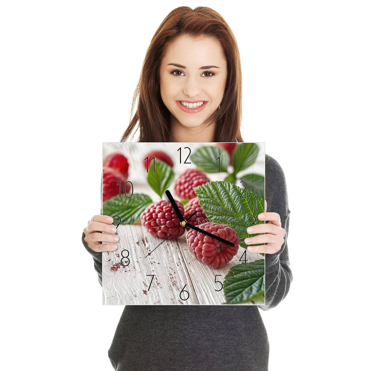 Quadratische Wanduhr aus Glas Himbeeren auf Weiß in zwei Händen gehalten – Größenvergleich, 30 × 30 cm