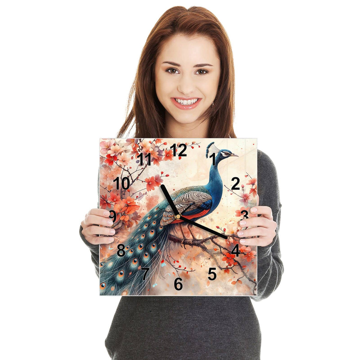 Quadratische Wanduhr aus Glas Pfau auf Kirschzweig in zwei Händen gehalten – Größenvergleich, 30 × 30 cm