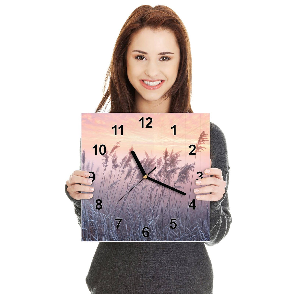 Quadratische Wanduhr aus Glas Schilf im Morgenrot in zwei Händen gehalten – Größenvergleich, 30 × 30 cm