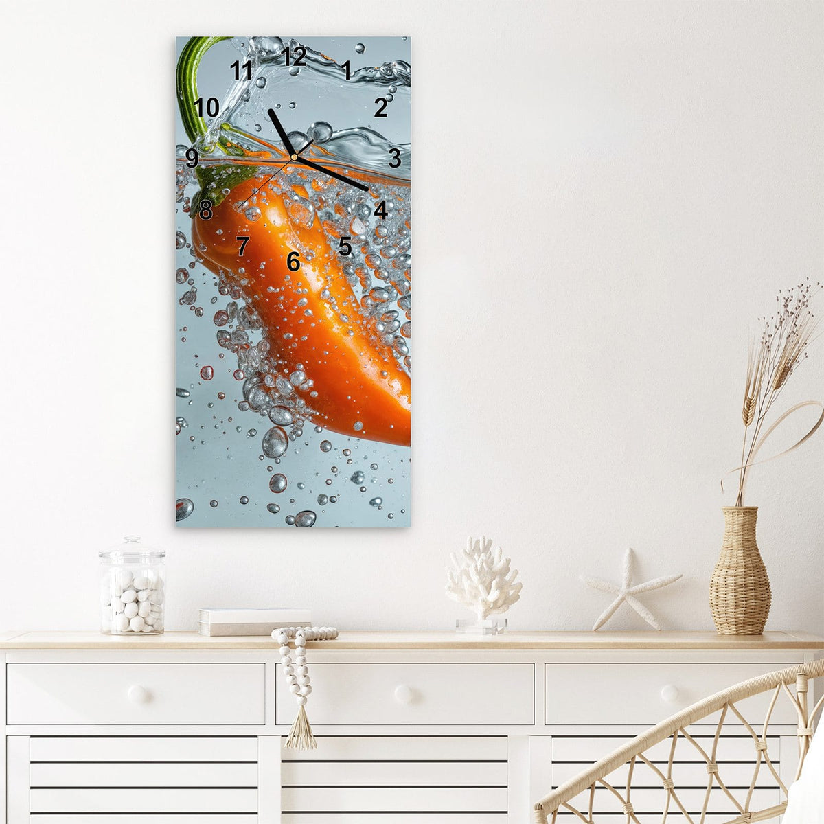 Wanduhr aus Glas im Hochformat Spritzige Paprika mit Ziffernblatt Modern über einem weißen Sideboard
