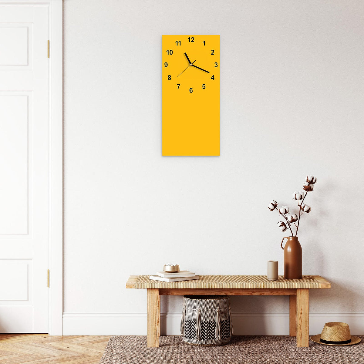 Wanduhr aus Glas im Hochformat Bernsteingelb mit Ziffernblatt Modern über einer Holzbank im Flur