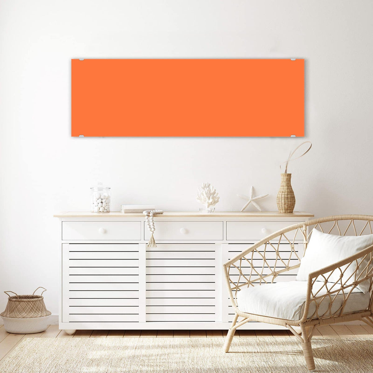 Wandbild aus Glas Korallenorange über einem weißen Sideboard neben einem Rattansessel