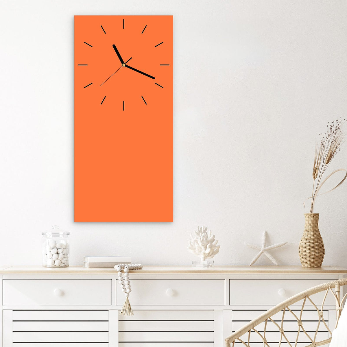 Wanduhr aus Glas im Hochformat Korallenorange mit Ziffernblatt Linie über einem weißen Sideboard