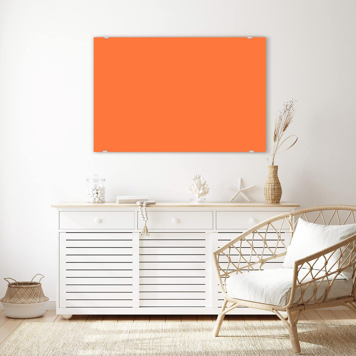 Wandbild aus Glas Korallenorange über einem weißen Sideboard neben einem Rattansessel