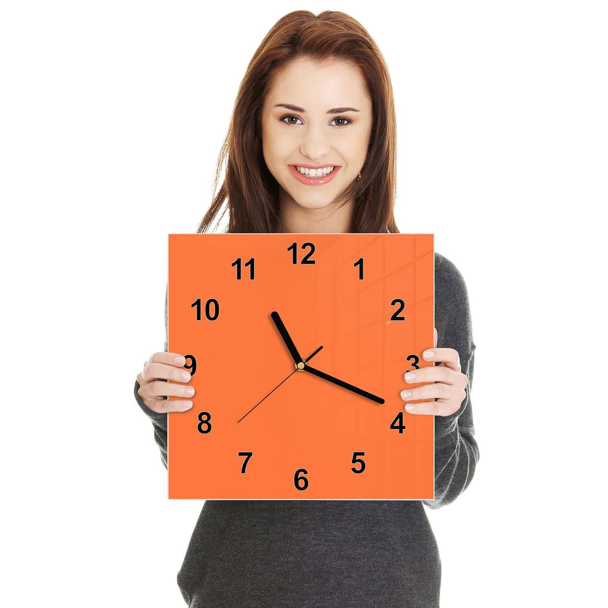 Quadratische Wanduhr aus Glas Korallenorange in zwei Händen gehalten – Größenvergleich, 30 × 30 cm