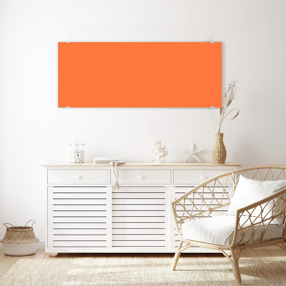 Wandbild aus Glas Korallenorange über einem weißen Sideboard neben einem Rattansessel