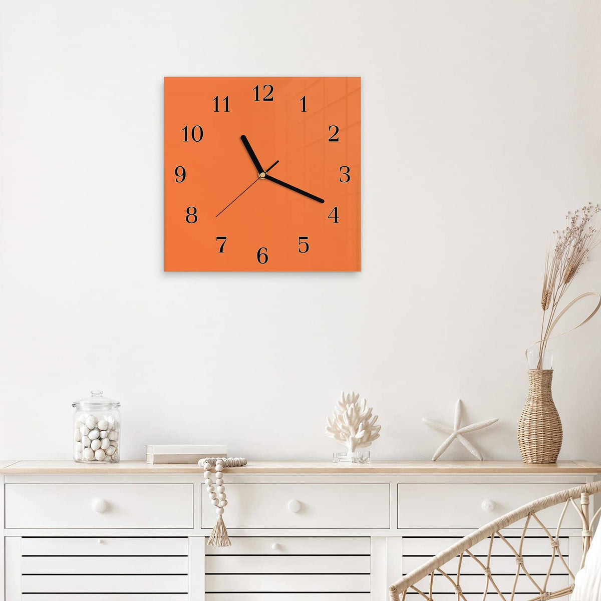 Quadratische Wanduhr aus Glas Korallenorange mit Ziffernblatt Klassisch über einem weißen Sideboard