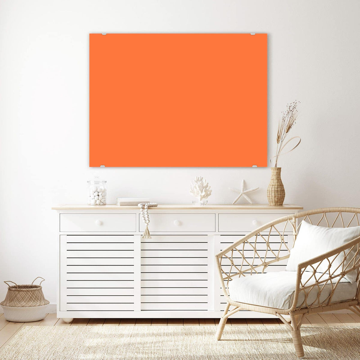 Wandbild aus Glas Korallenorange über einem weißen Sideboard neben einem Rattansessel