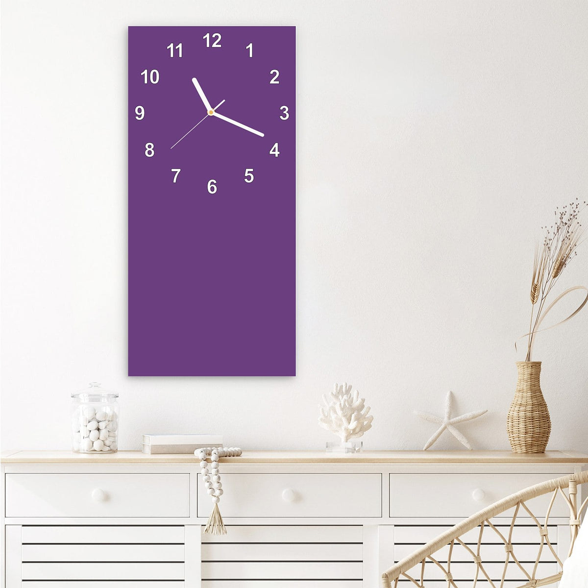 Wanduhr aus Glas im Hochformat Pflaumenlila mit Ziffernblatt Modern über einem weißen Sideboard