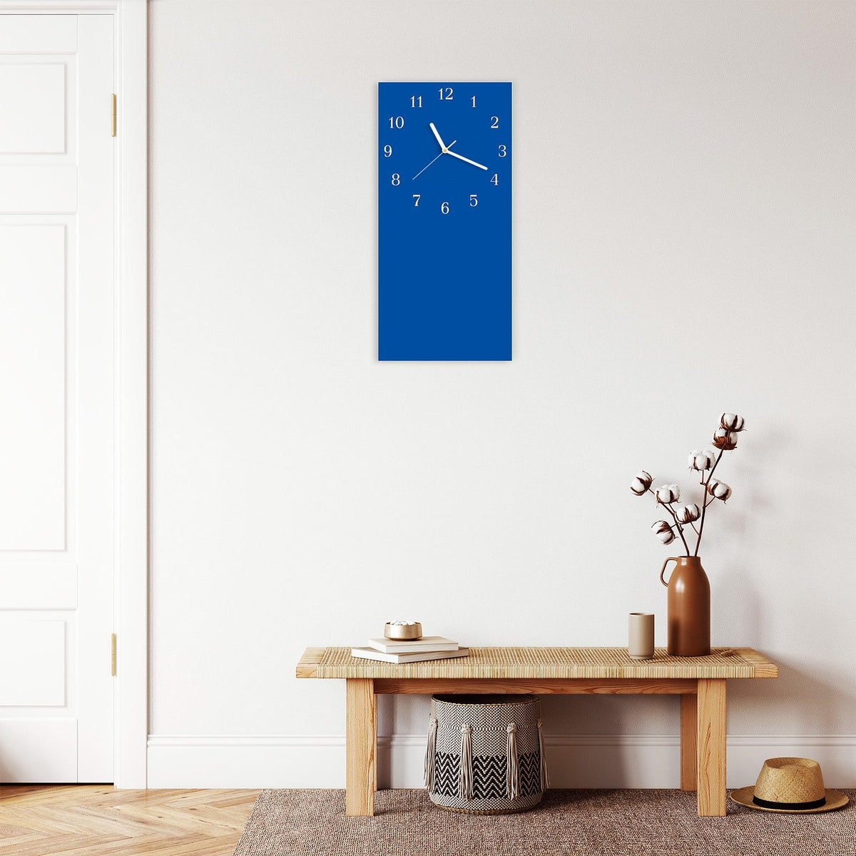Wanduhr aus Glas im Hochformat Signalblau mit Ziffernblatt Klassisch über einer Holzbank im Flur