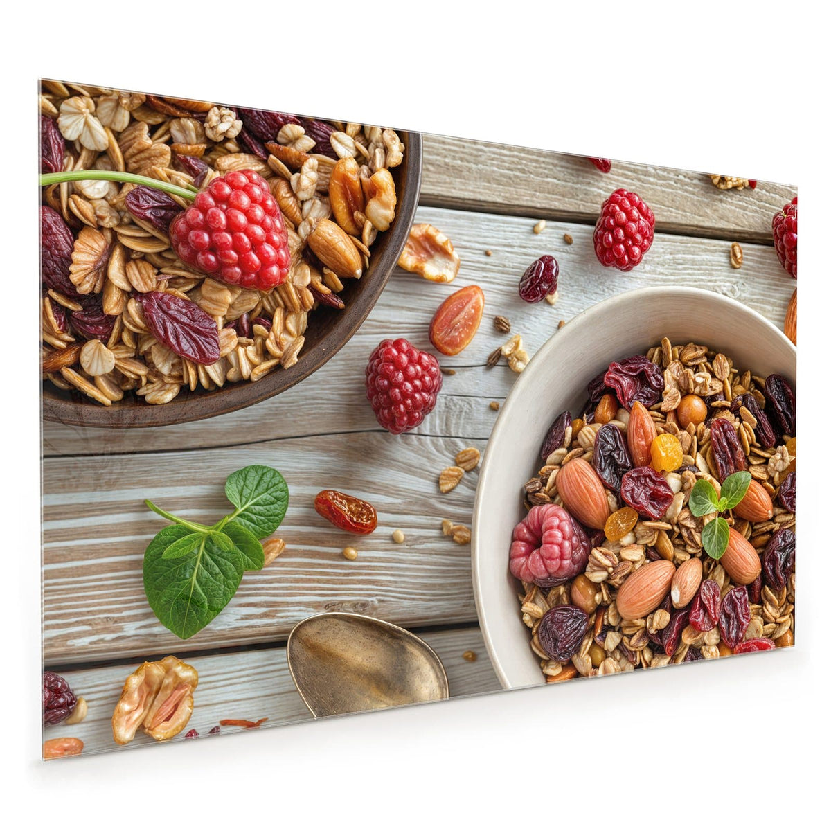 Küchenrückwand aus Glas im Hochformat: Schale mit Granola, Mandeln, Nüssen, Cranberrys und Rosinen auf hellem Holz, dazu Himbeeren, Löffel