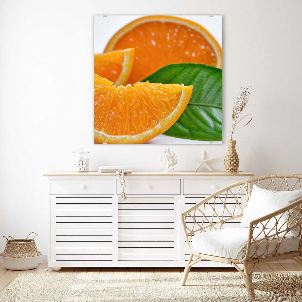 Glasbild Orangenscheiben an der Wand – Saftige Orangenspalten und eine halbe Orange mit großem grünem Blatt vor Weiß