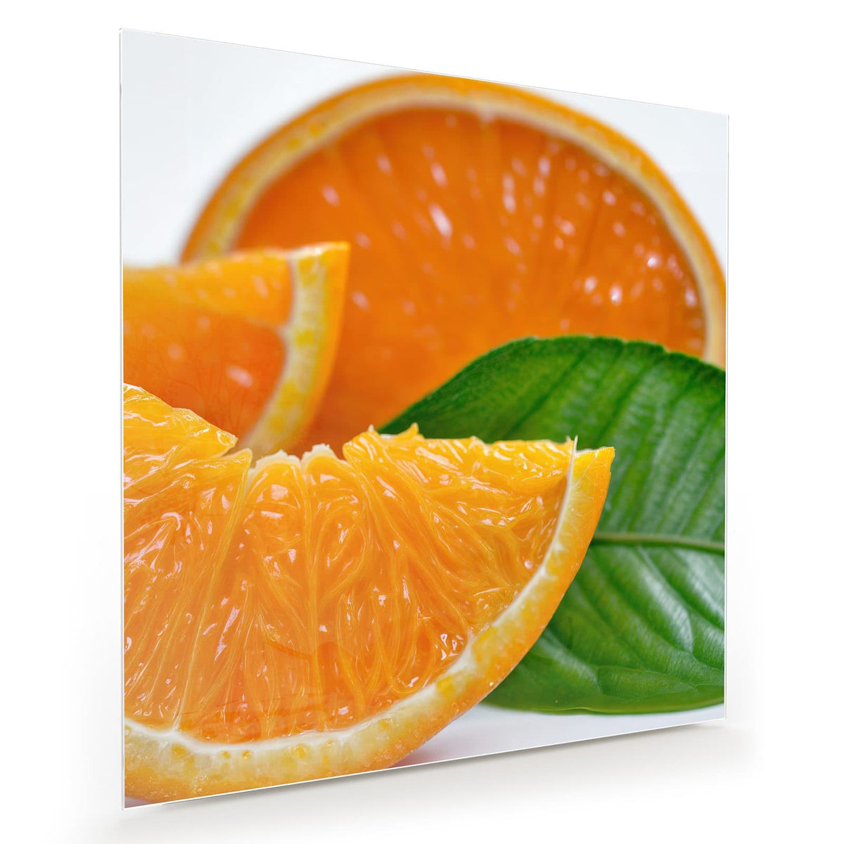 Saftige Orangenspalten und eine halbe Orange mit großem grünem Blatt vor Weiß