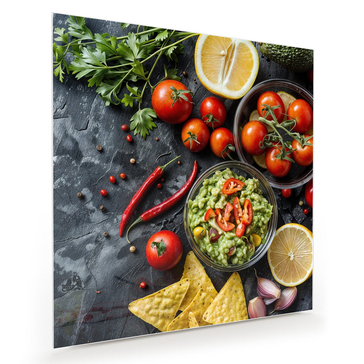 Schale Guacamole mit Chili, dazu Tomaten, Zitronen, Petersilie und Tortillachips auf Schiefer