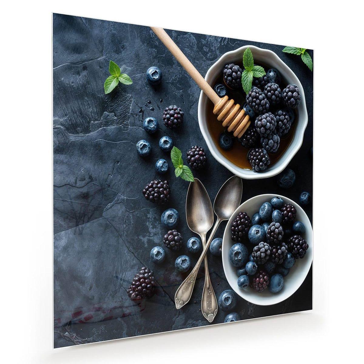 Zwei weiße Schalen mit Heidel- und Brombeeren, Honig mit Honiglöffel, Minze und alte Löffel auf dunklem Schiefer.