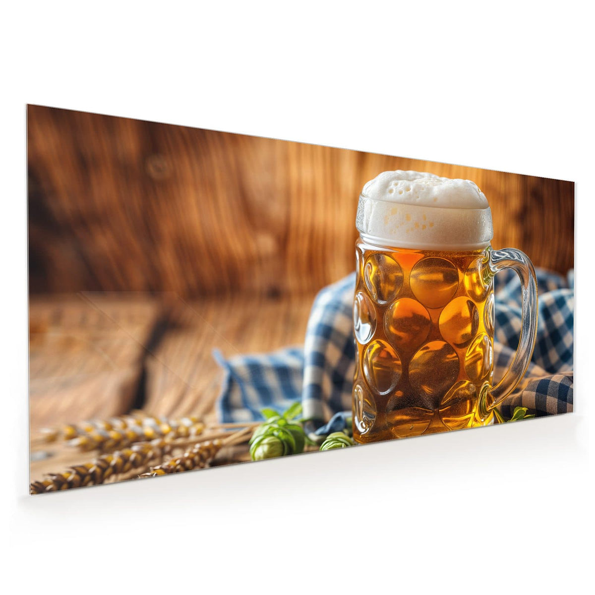 Gedellter Glaskrug mit goldenem Bier und hoher Schaumkrone, davor Hopfendolden, dahinter ein blau-weiß kariertes Tuch.