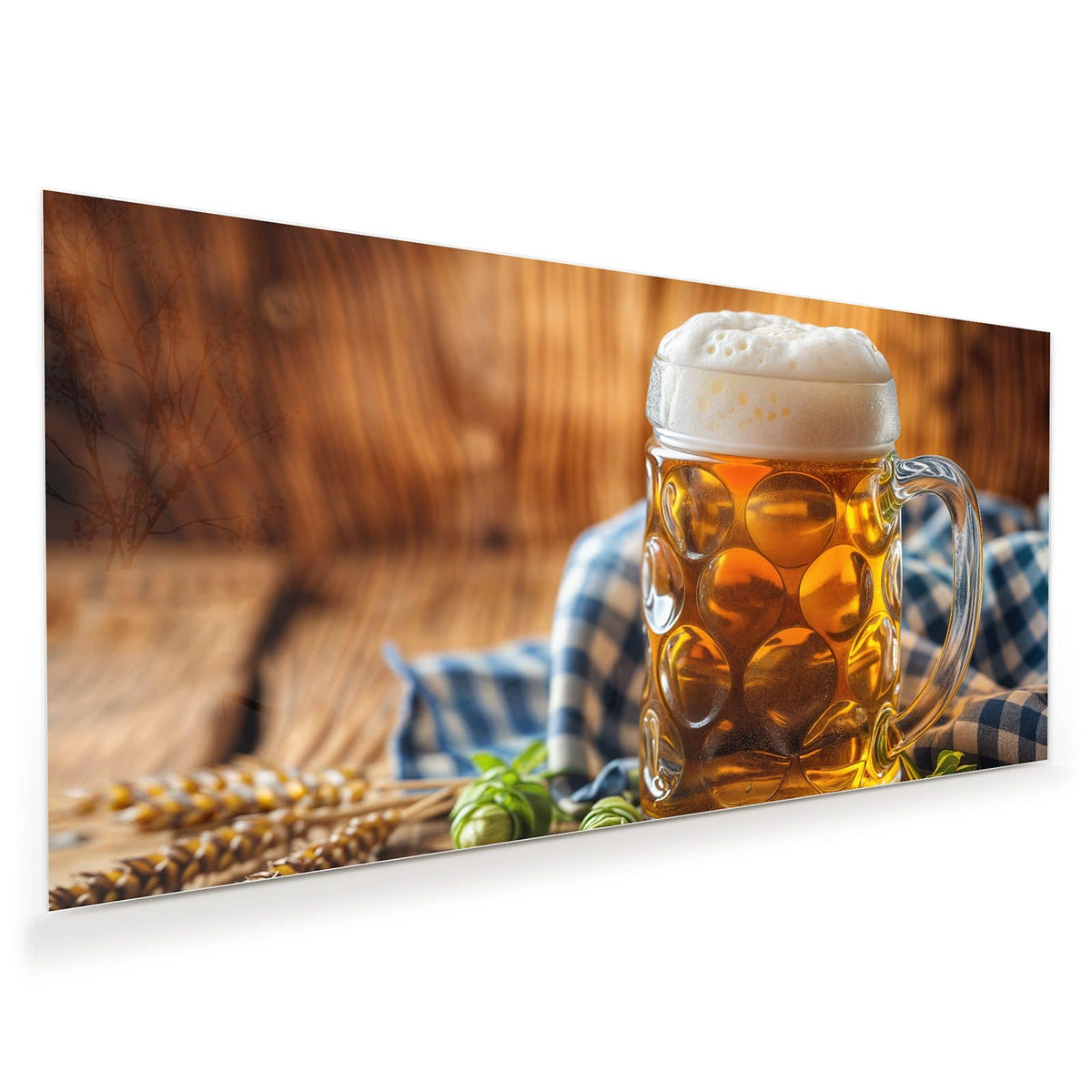 Gedellter Glaskrug mit goldenem Bier und hoher Schaumkrone, davor Hopfendolden, dahinter ein blau-weiß kariertes Tuch.