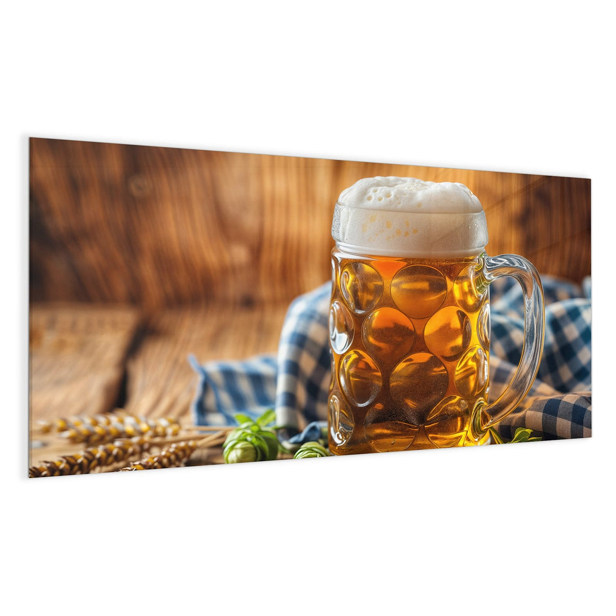 Gedellter Glaskrug mit goldenem Bier und hoher Schaumkrone, davor Hopfendolden, dahinter ein blau-weiß kariertes Tuch.