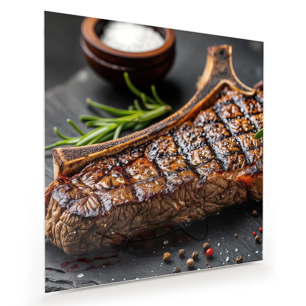 Angeschnittenes T-Bone-Steak mit Grillstreifen auf Schiefer, dazu Rosmarin, Salzschale und Pfefferkörner