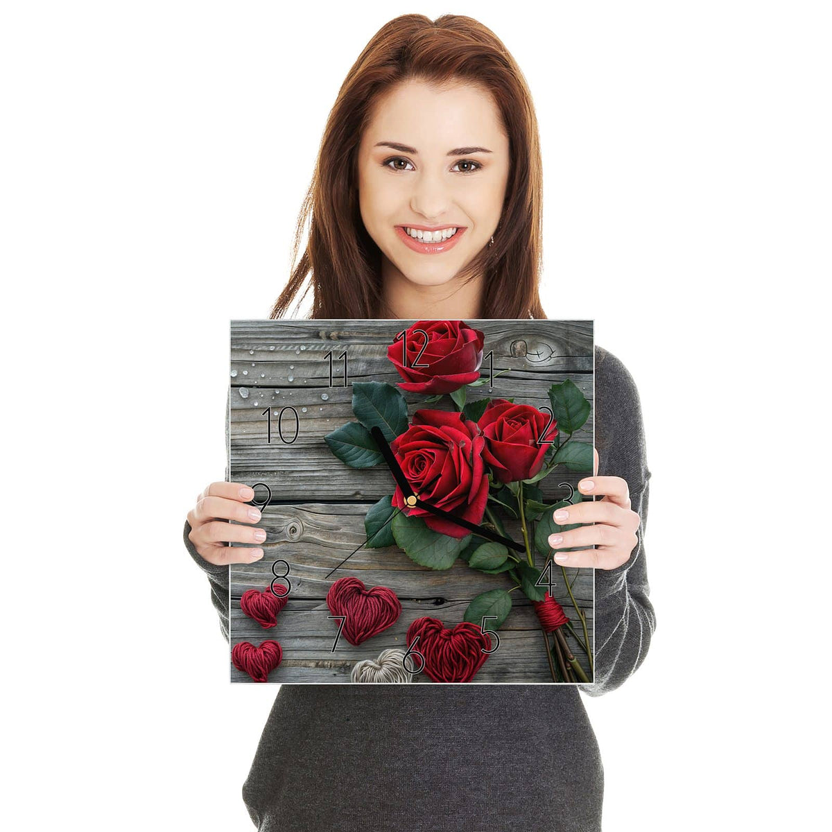Drei tiefrote Rosen mit Blättern auf grauen Holzdielen, darunter vier aus rotem und beigem Garn gewickelte Herzen