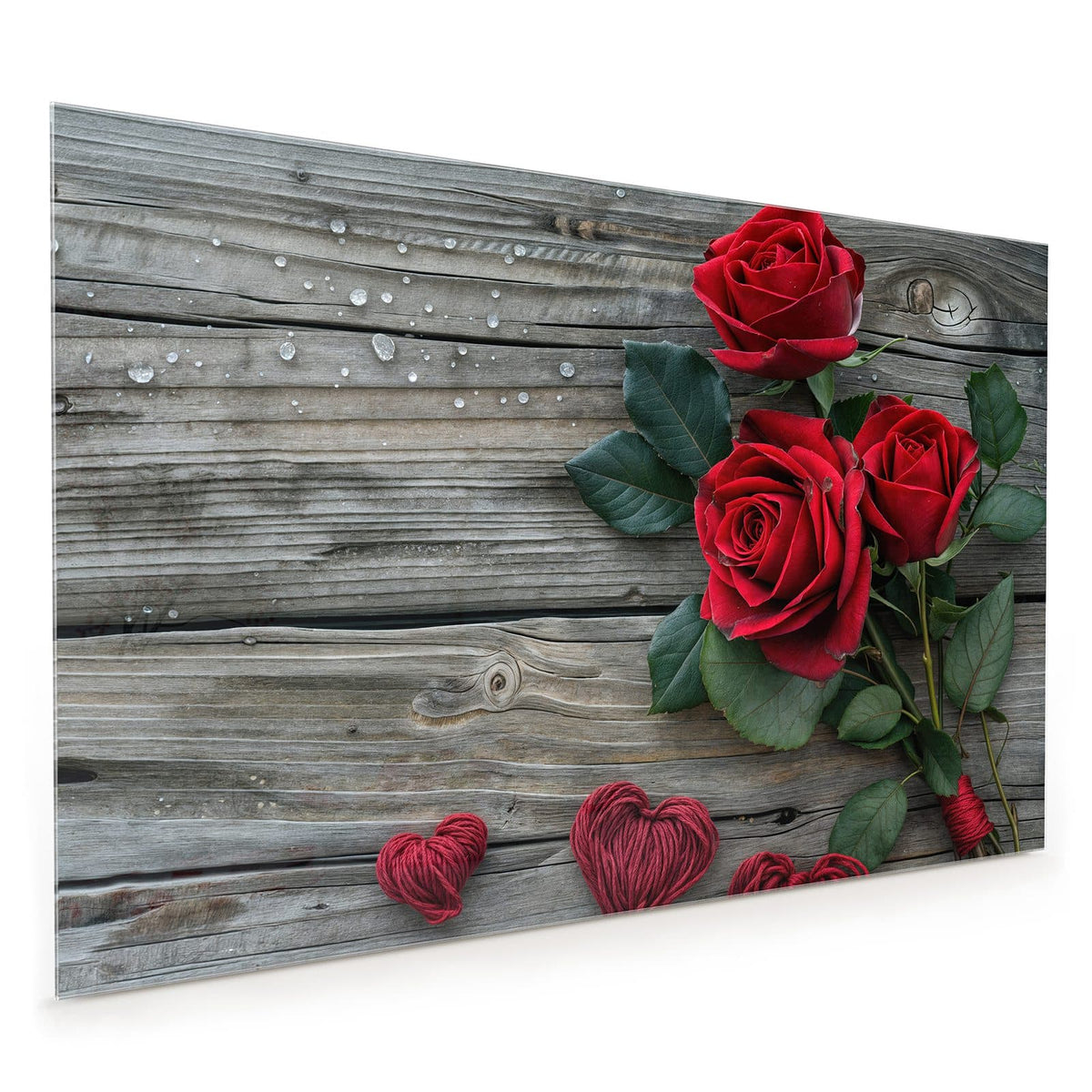 Küchenrückwand aus Glas im Hochformat: Drei tiefrote Rosen mit Blättern auf grauen Holzdielen, darunter vier aus rotem und beigem Garn gewickelte Herzen