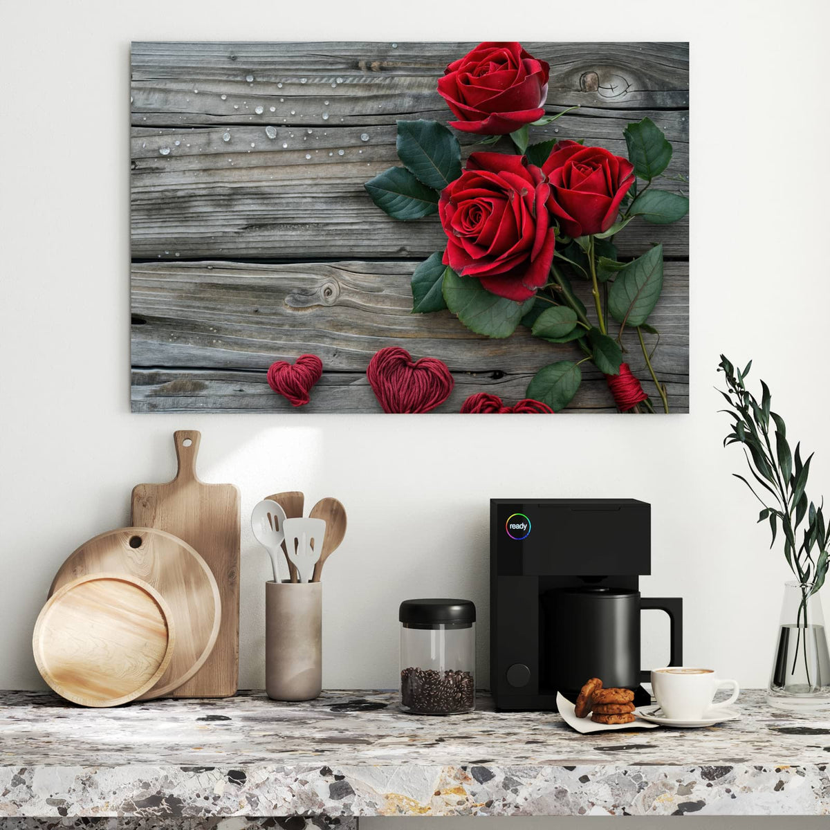 Drei tiefrote Rosen mit Blättern auf grauen Holzdielen, darunter vier aus rotem und beigem Garn gewickelte Herzen