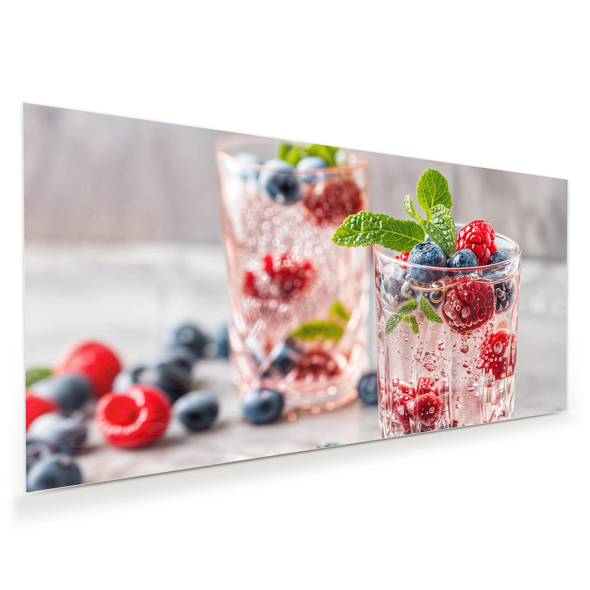 Zwei geschliffene Gläser mit perlender rosa Limonade, Himbeeren, Blaubeeren und Minze obenauf.