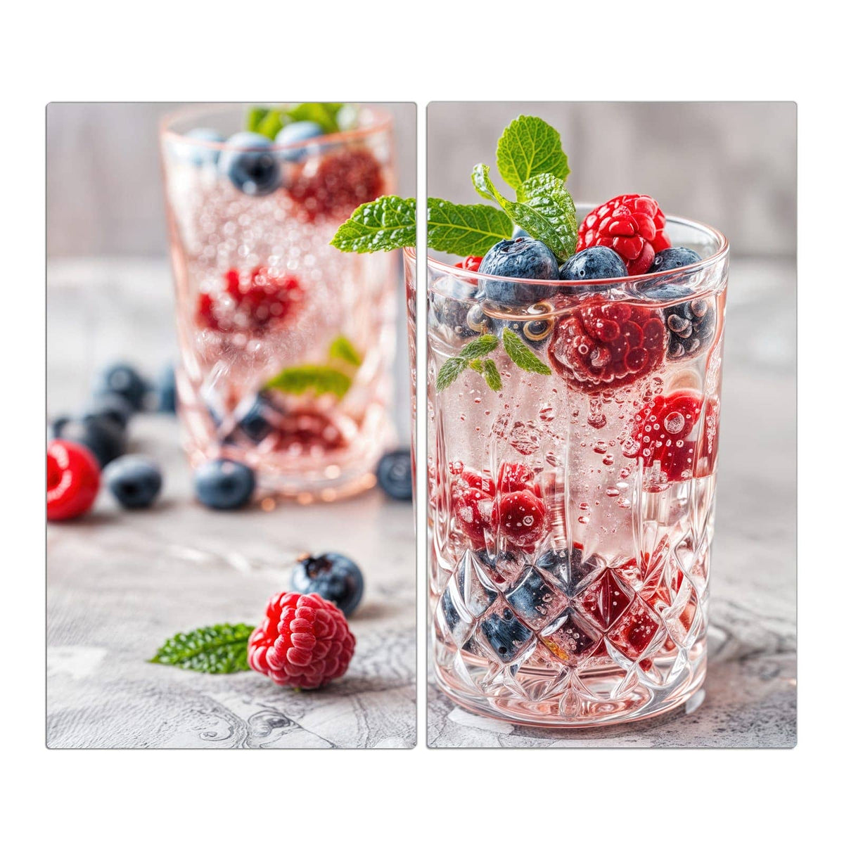 Zwei geschliffene Gläser mit perlender rosa Limonade, Himbeeren, Blaubeeren und Minze obenauf.