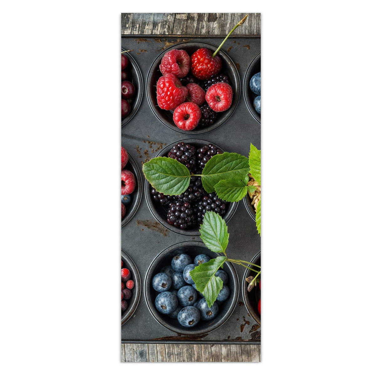 Muffinblech, dessen Mulden mit Kirschen, Himbeeren, Blaubeeren, Brombeeren, Johannisbeeren und Haferflocken gefüllt sind, auf Holz