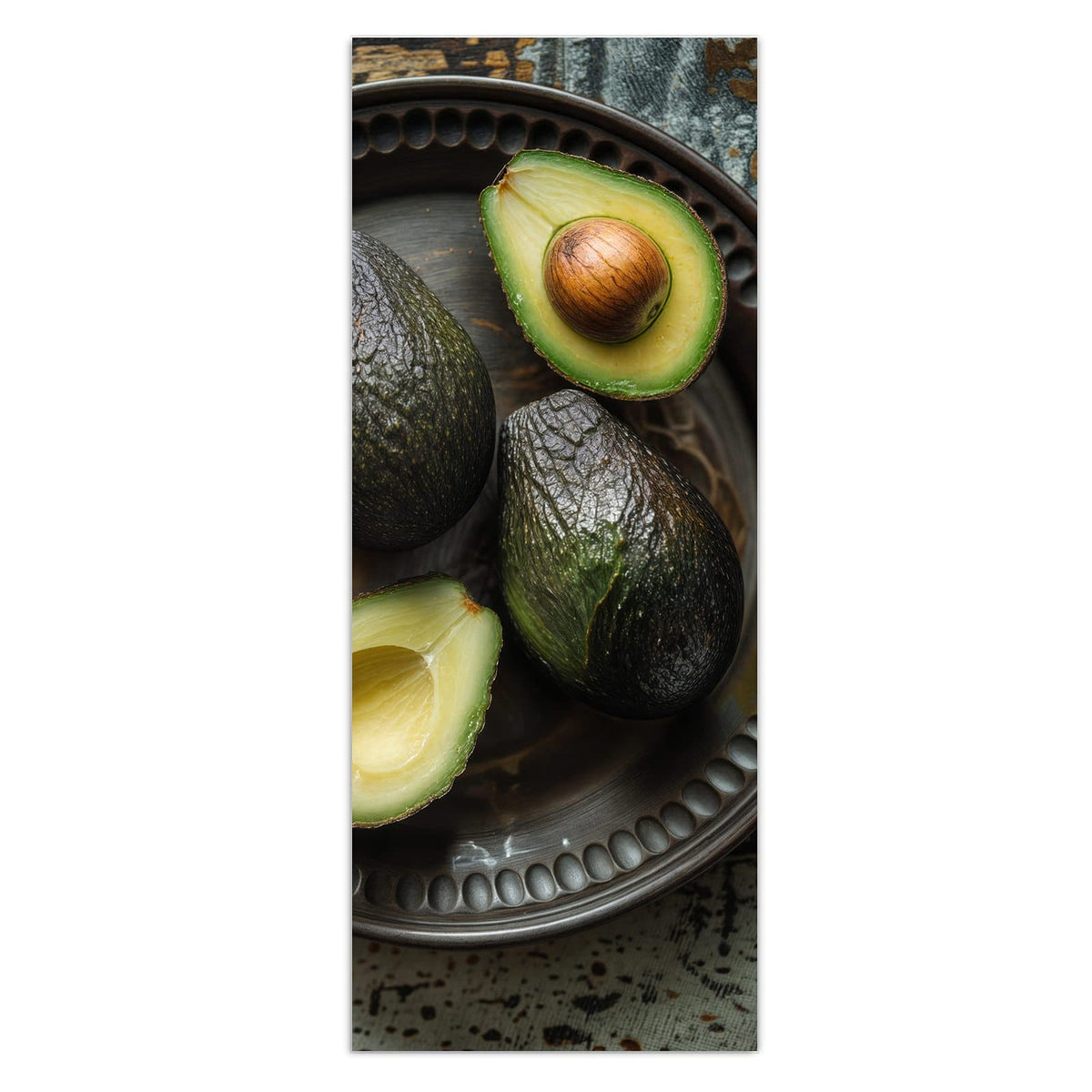 Vier Avocados, zwei davon halbiert, auf dunklem Metallteller mit Perlrand auf verwittertem Holz