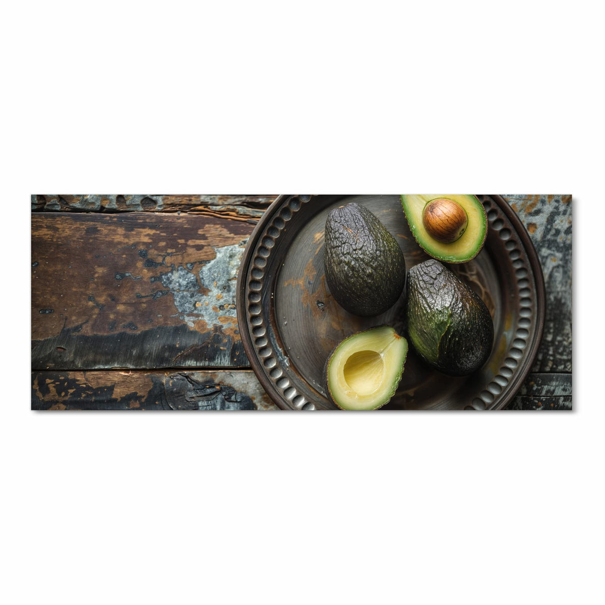 Vier Avocados, zwei davon halbiert, auf dunklem Metallteller mit Perlrand auf verwittertem Holz