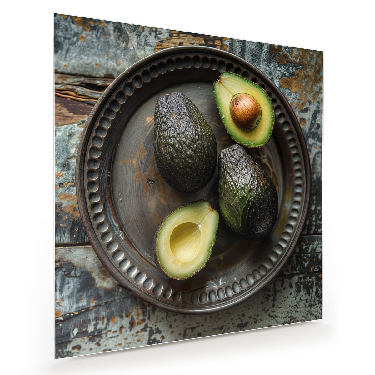 Vier Avocados, zwei davon halbiert, auf dunklem Metallteller mit Perlrand auf verwittertem Holz