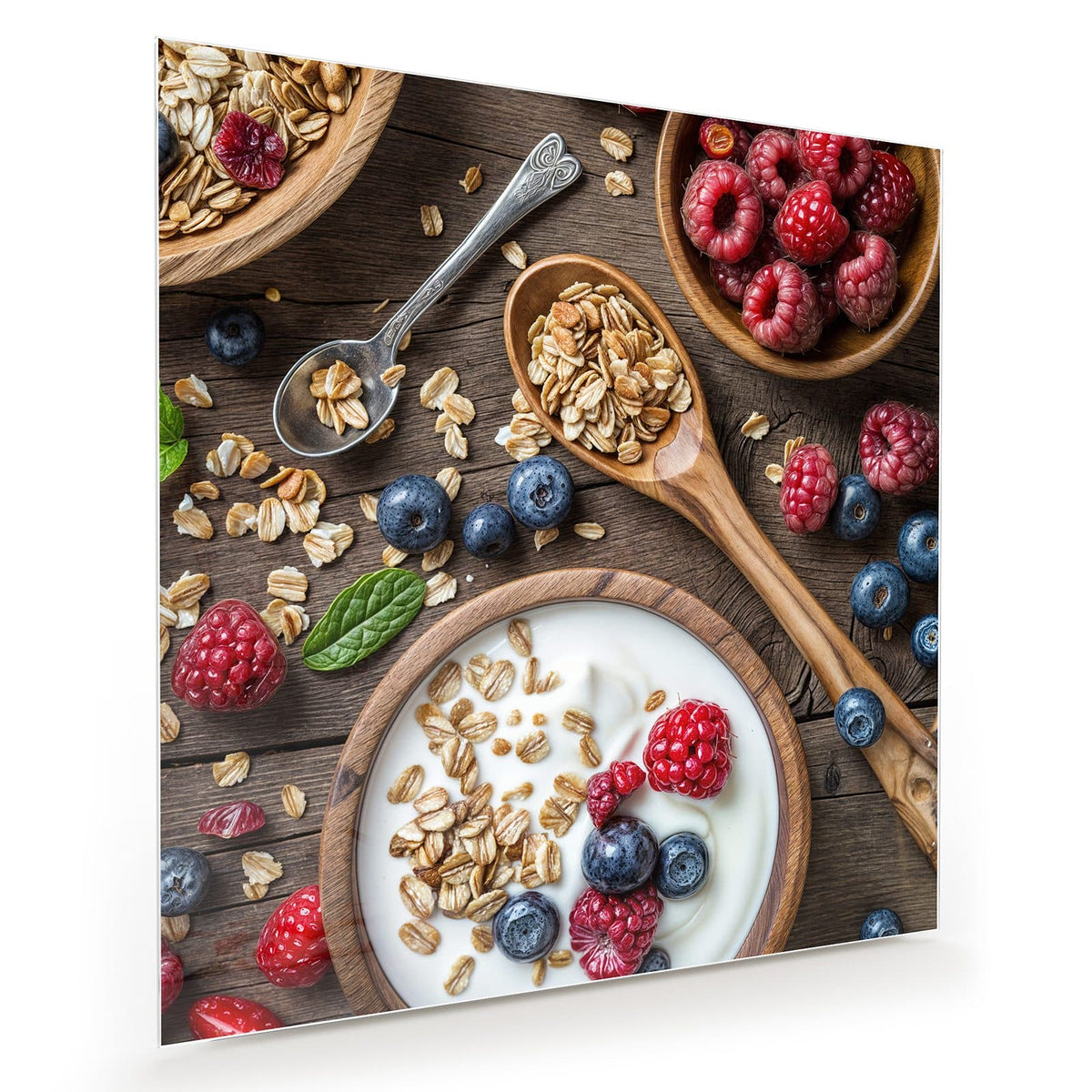Schale mit Joghurt, Haferflocken, Himbeeren und Blaubeeren, Holzlöffel auf Holztisch