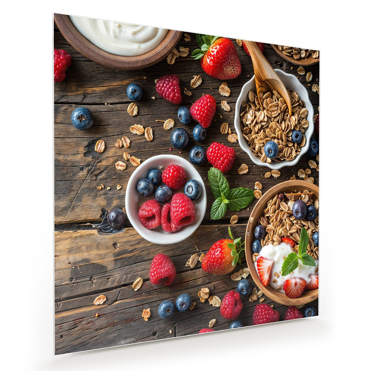 Draufsicht auf dunkles Holz: Schalen mit Granola, eine Schale Joghurt, Joghurt mit Erdbeeren, dazu Himbeeren, Blaubeeren und Holzlöffel.