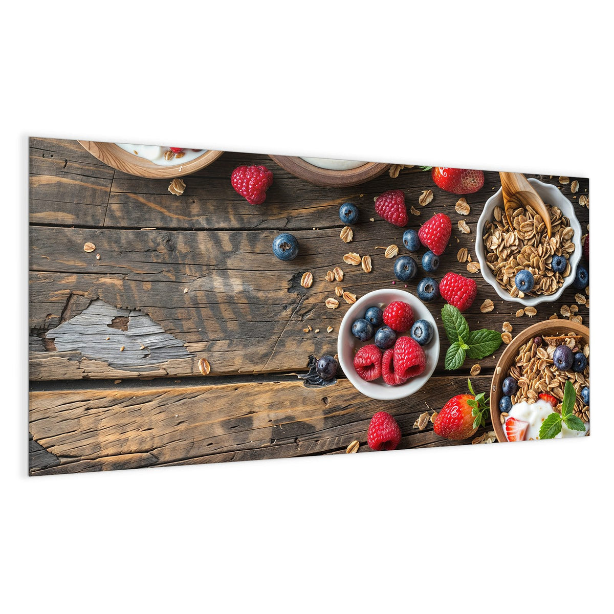 Draufsicht auf dunkles Holz: Schalen mit Granola, eine Schale Joghurt, Joghurt mit Erdbeeren, dazu Himbeeren, Blaubeeren und Holzlöffel.