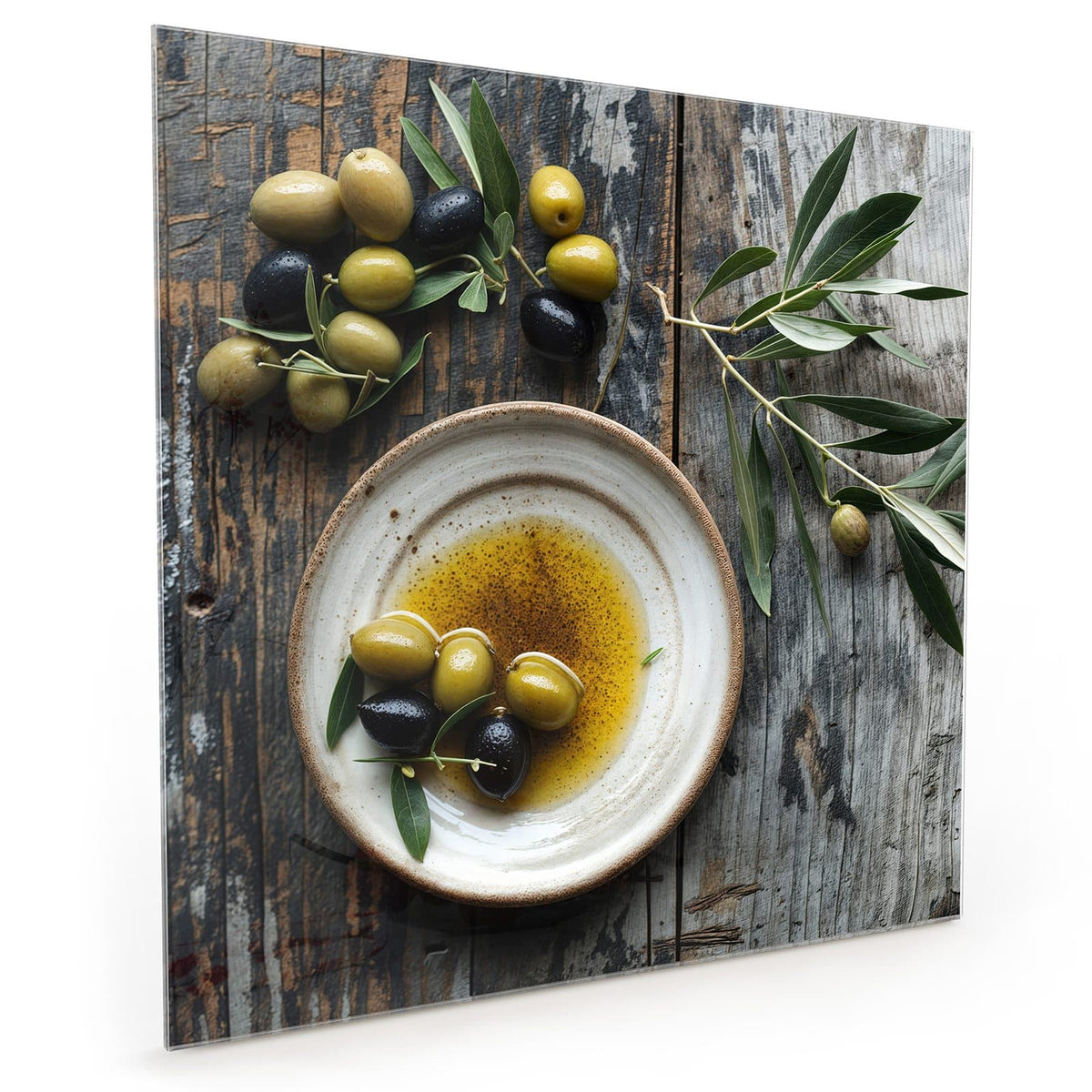 Küchenrückwand aus Glas im quadratischen Format: Flacher Keramikteller mit Olivenöl und grünen wie schwarzen Oliven, dazu Olivenzweige auf Holz #grösse_40 x 40 cm #grösse_50 x 50 cm #grösse_60 x 60 cm