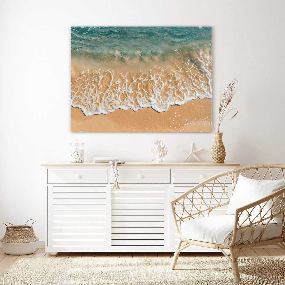 Wandbild aus Glas Meeresschaum auf Sand über einem weißen Sideboard neben einem Rattansessel
