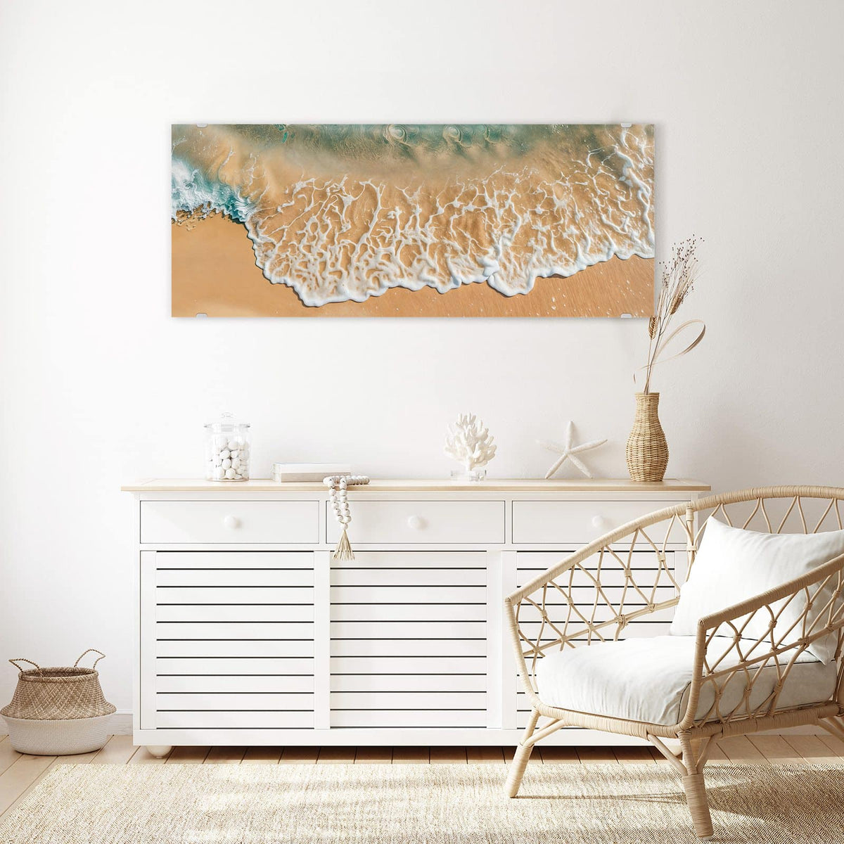 Wandbild aus Glas Meeresschaum auf Sand über einem weißen Sideboard neben einem Rattansessel