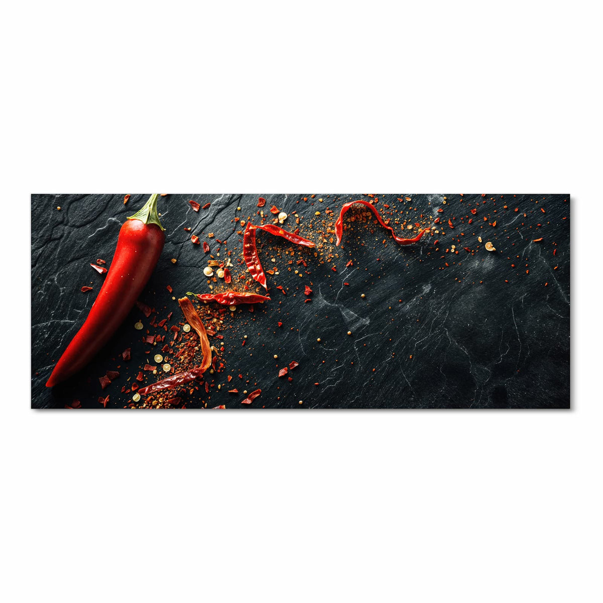 Eine rote Chilischote auf dunkler Schieferplatte, daneben getrocknete Schotenstücke und Flocken