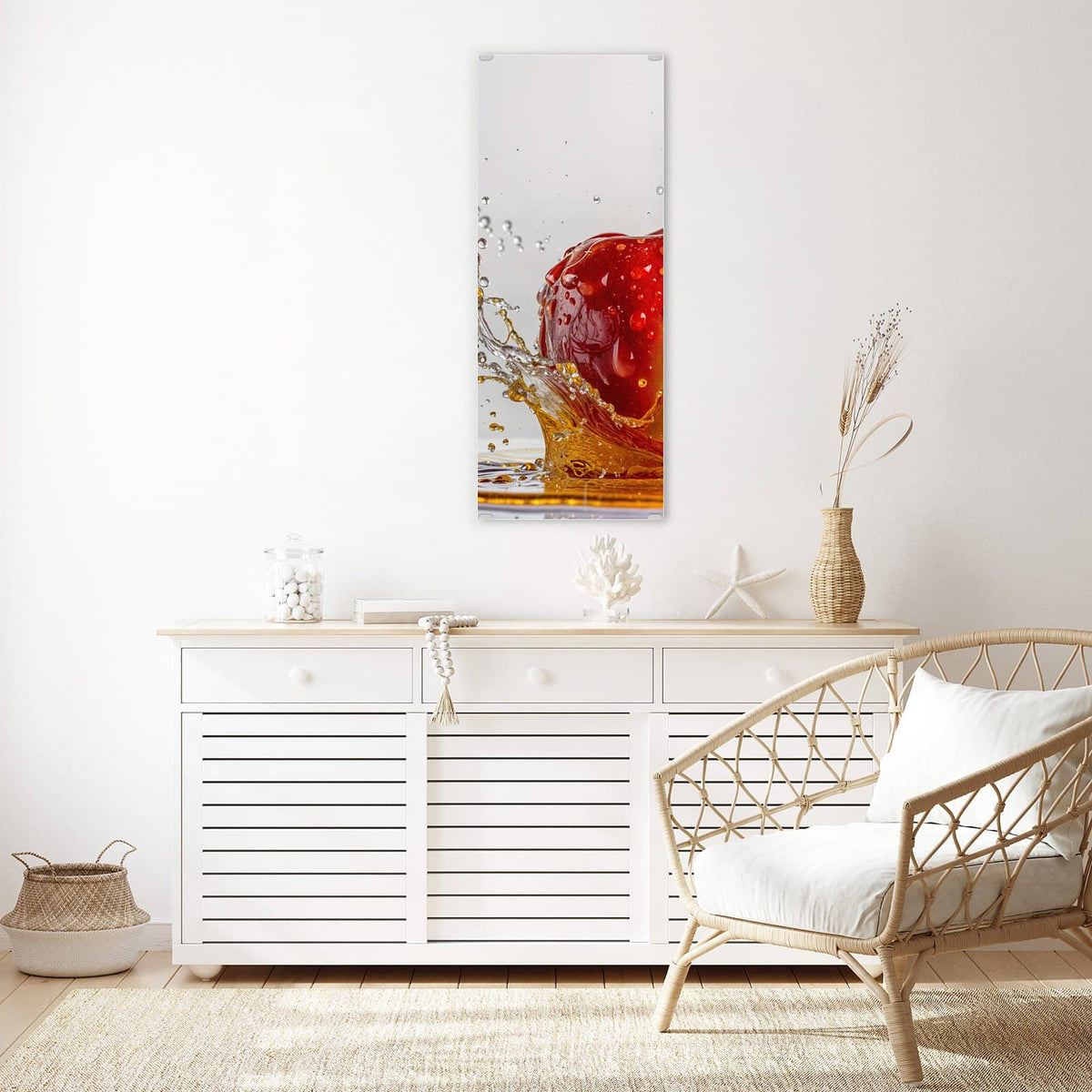 Wandbild aus Glas Apfel mit Saftspritzer über einem weißen Sideboard neben einem Rattansessel