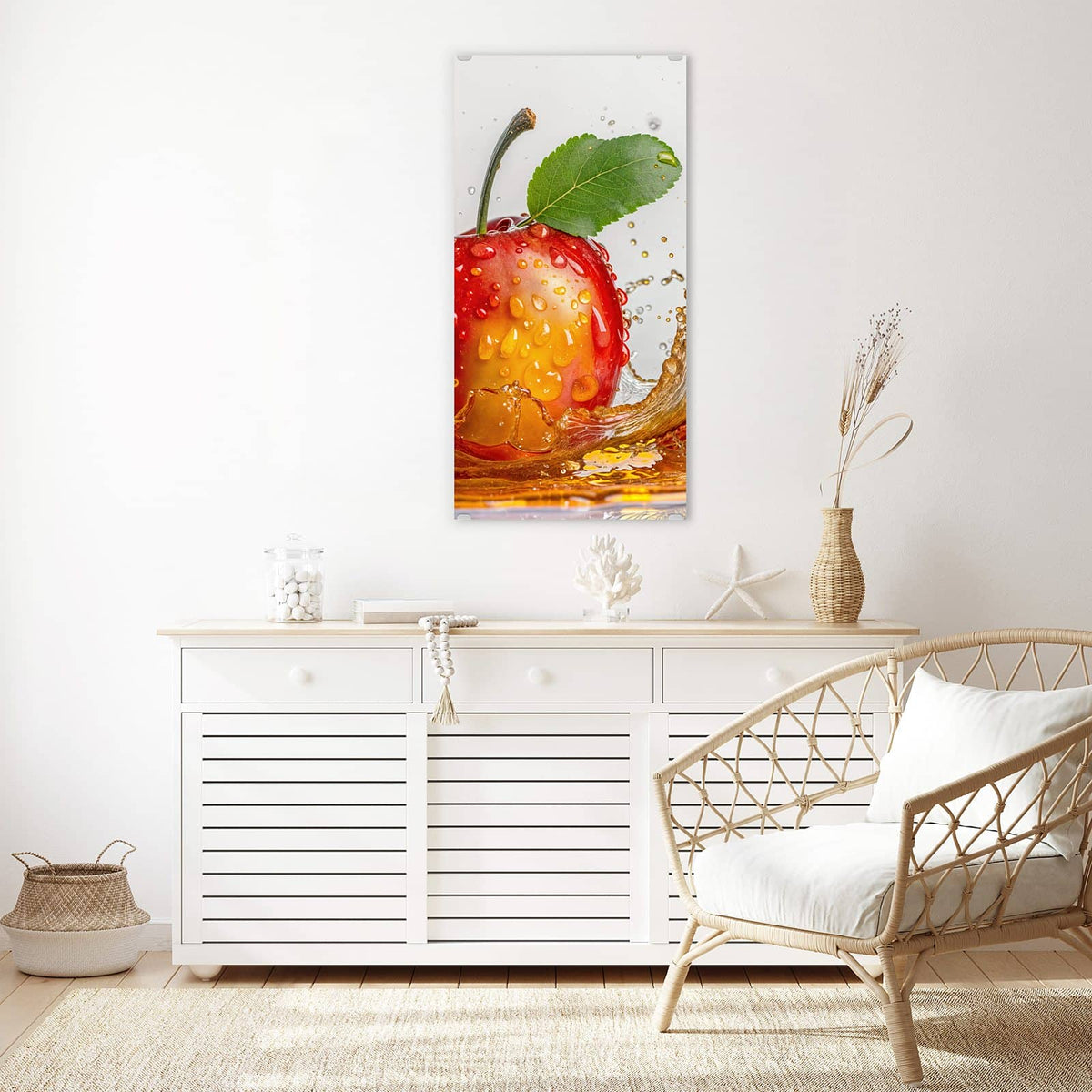 Wandbild aus Glas Apfel mit Saftspritzer über einem weißen Sideboard neben einem Rattansessel