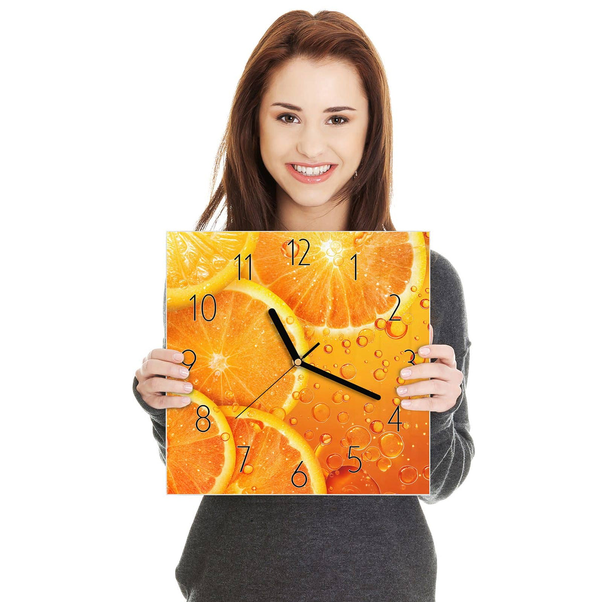 Quadratische Wanduhr aus Glas Sprudelnde Orangen in zwei Händen gehalten – Größenvergleich, 30 × 30 cm