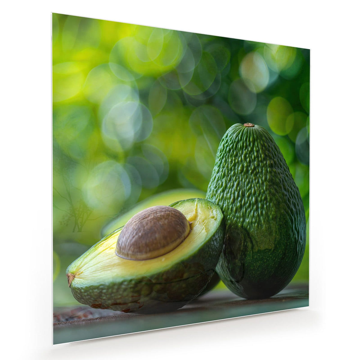 Halbierte Avocado mit Kern vor einer ganzen Avocado, grünes Bokeh im Hintergrund