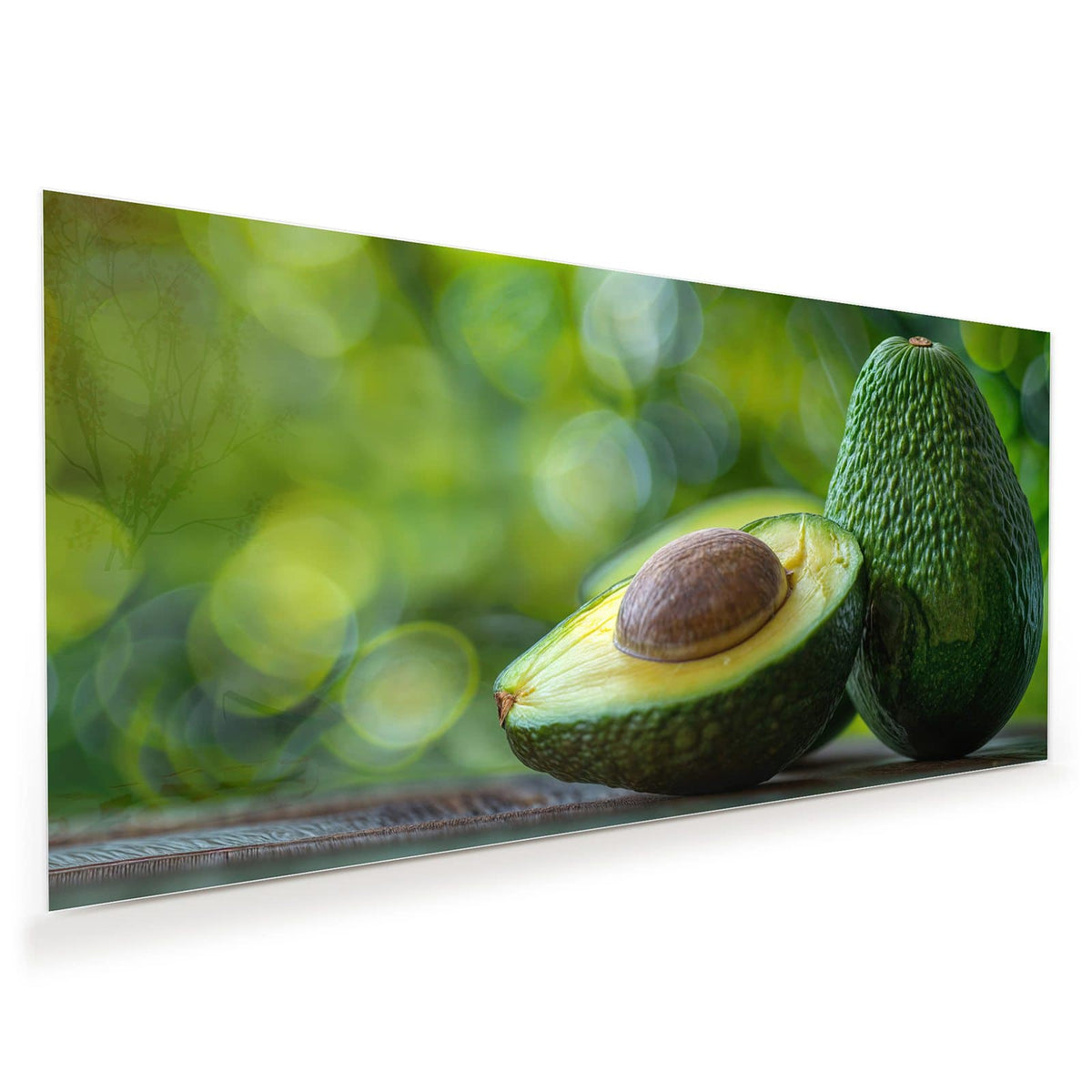 Halbierte Avocado mit Kern vor einer ganzen Avocado, grünes Bokeh im Hintergrund