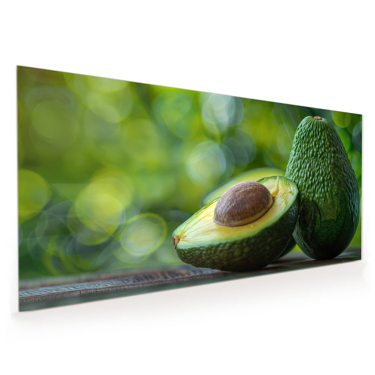 Küchenrückwand aus Glas im Hochformat: Halbierte Avocado mit Kern vor einer ganzen Avocado, grünes Bokeh im Hintergrund