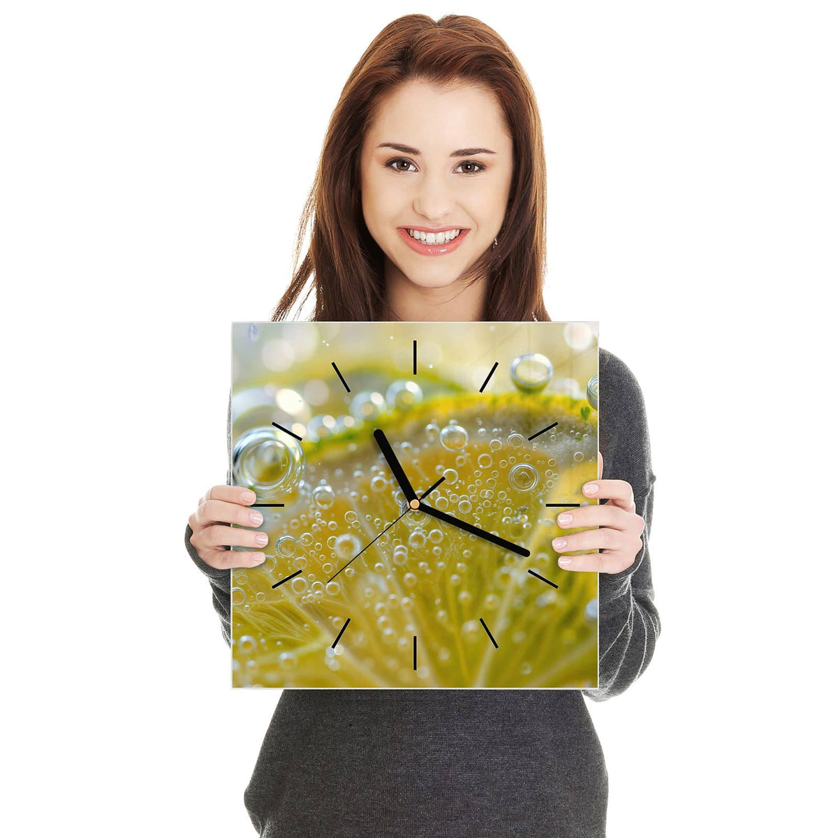 Quadratische Wanduhr aus Glas Zitrone im Sprudel in zwei Händen gehalten – Größenvergleich, 30 × 30 cm